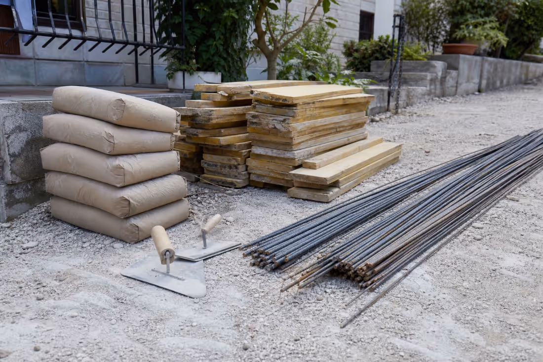Materiali za betonske stopnice: vreče cementa, lesena oplatitev, armaturno jeklo in gladilo za končno obdelavo.