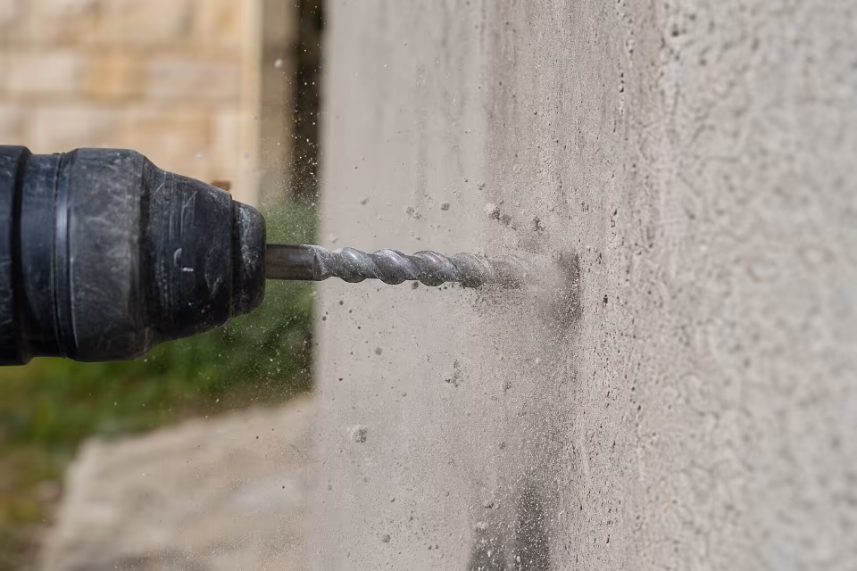 Detalj bušenja betona: vrh svrdla prodire u zid uz oblak prašine