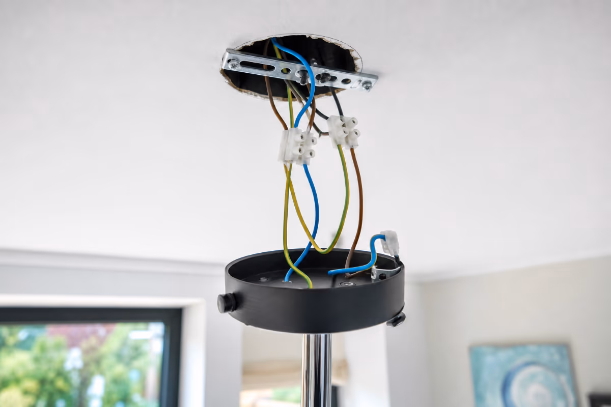 Instalacija električnih žica za svjetiljku na stropu s vidljivim spojevima i metalnim nosačem.
