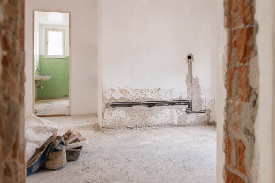 Majstor radi na zidu u stanu dok vlasnik posmatra, što simbolizuje nadzor i odgovornost tokom radova. — širi prikaz