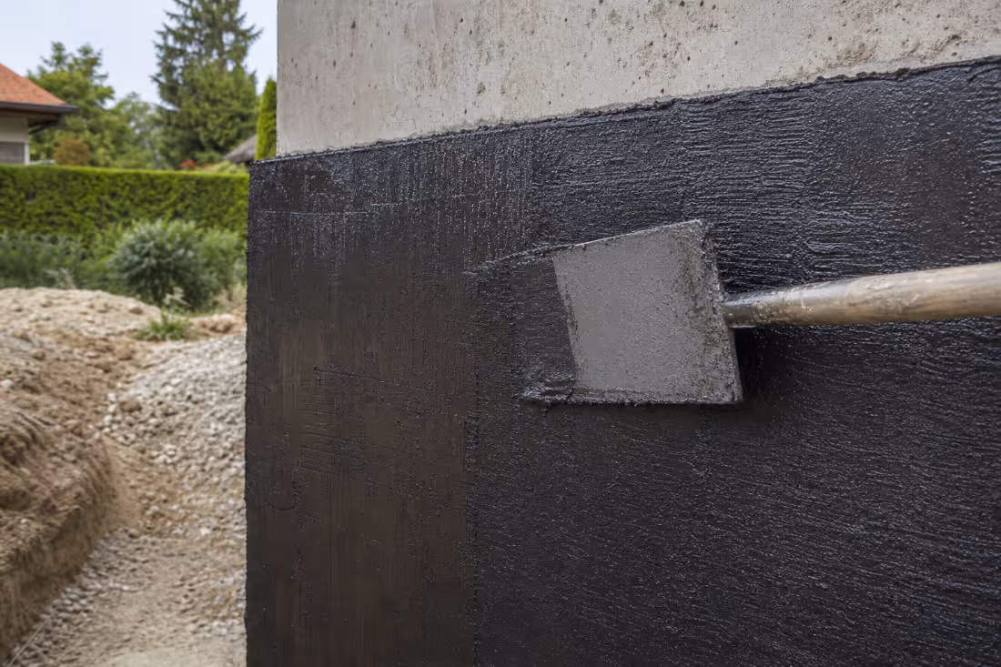 Detalj nanošenja crne hidroizolacijske membrane na betonski zid temelja podruma.