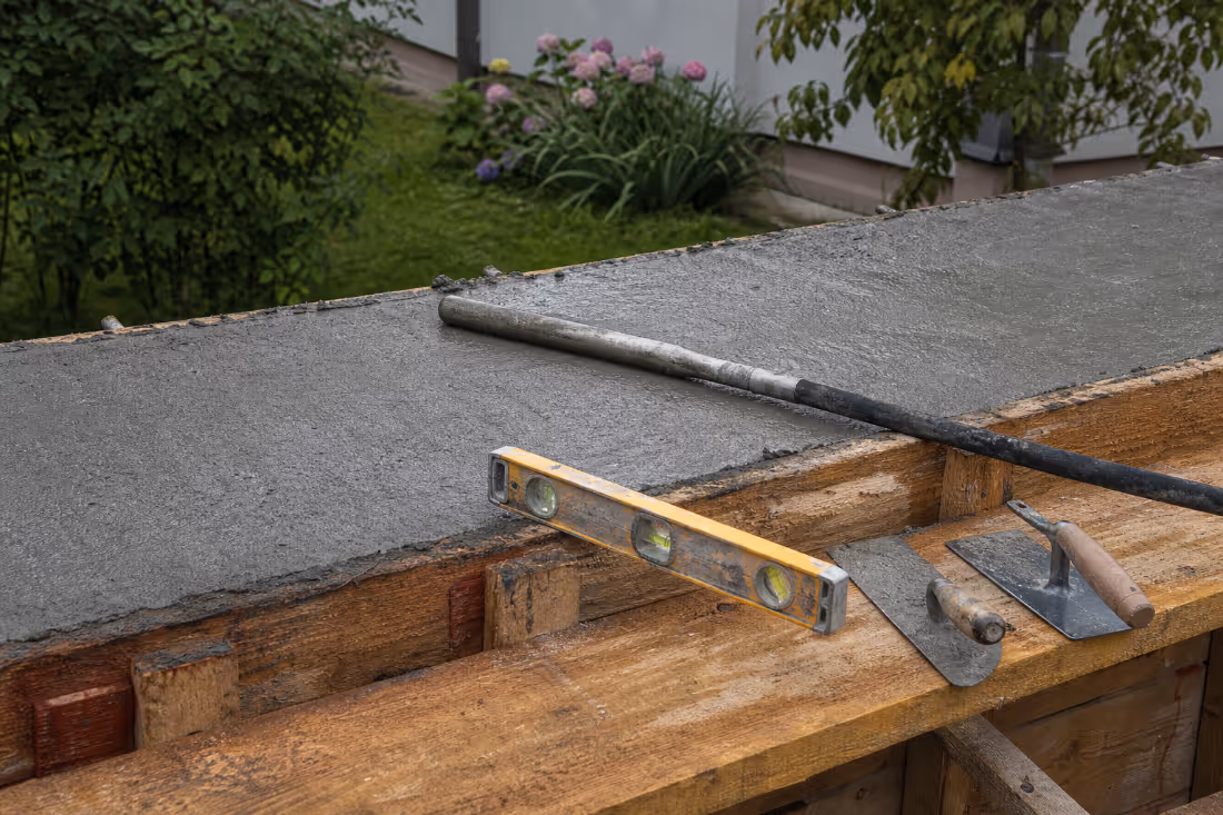 Alati za betoniranje na drvenoj oplati uz sveže izliveni rub betonske ploče, verovatno terase.
