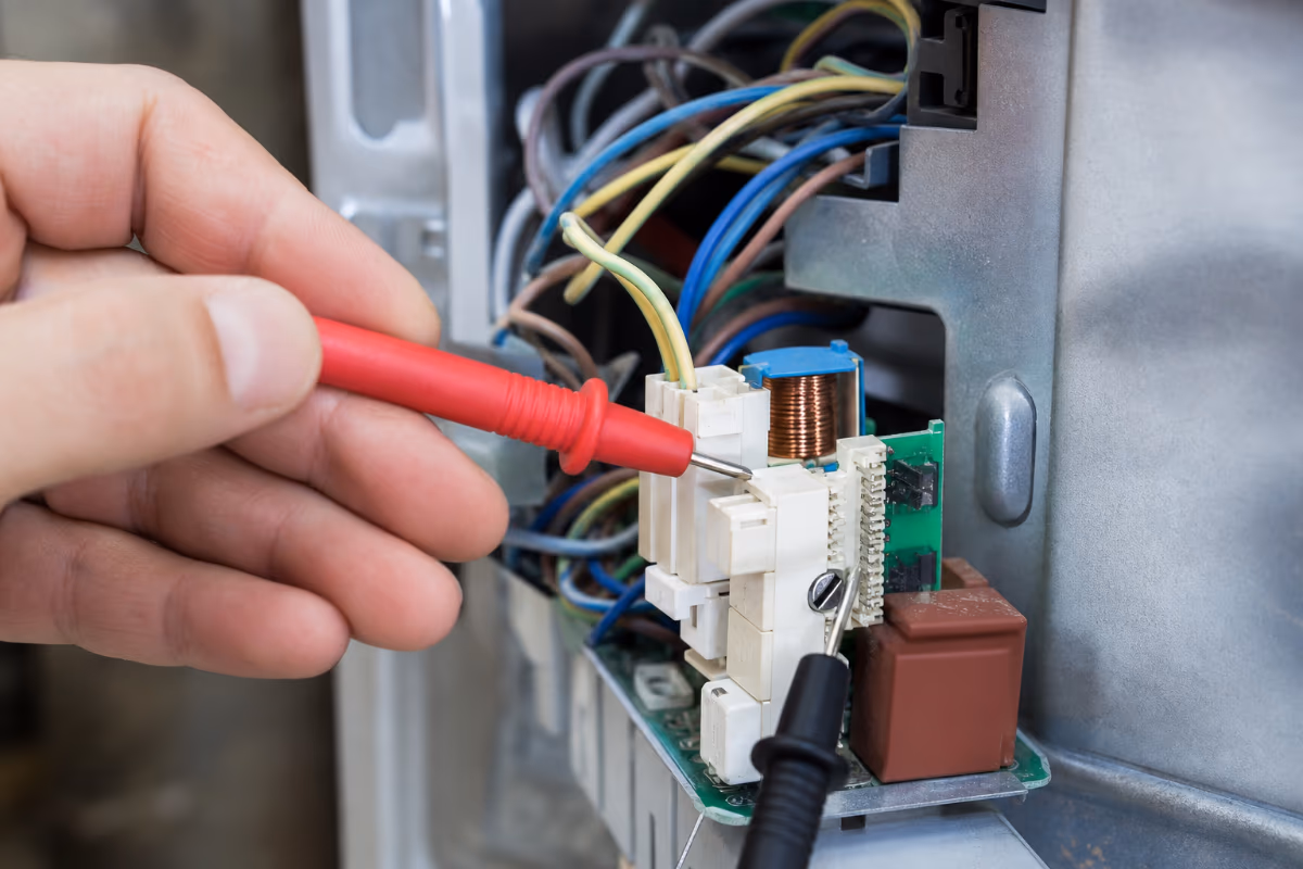 Tehnik z multimetrom diagnosticira elektroniko štedilnika, kar je ključni korak pri oceni cene popravila.