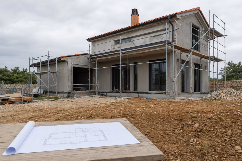 Arhitektonski projekt kuće na stolu ispred kuće u izgradnji s košarama i skeletom