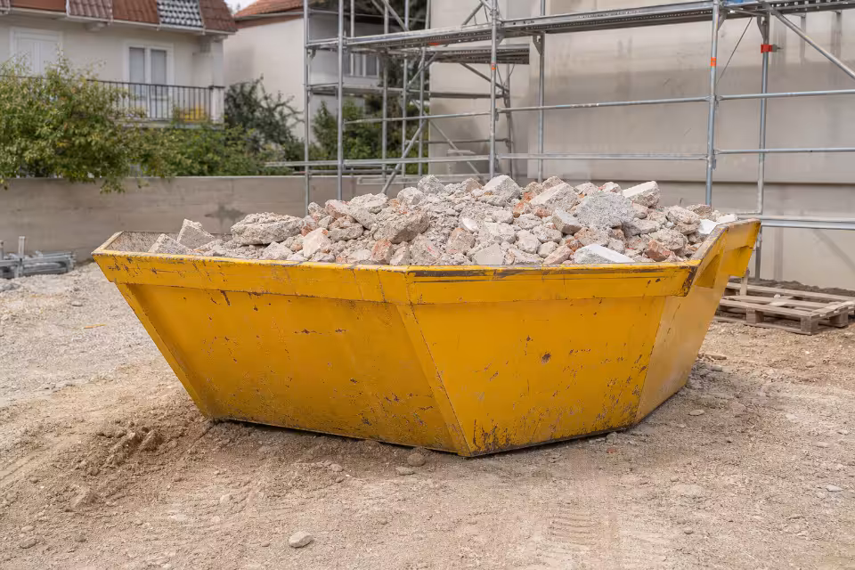 Žuti kontejner za građevinski otpad pun ruševina na gradilištu uz skele