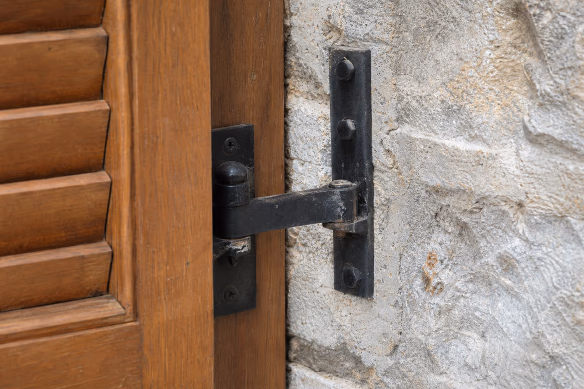 Detalj crnog metalnog okova koji drži drvenu šatoru na kamenom zidu.