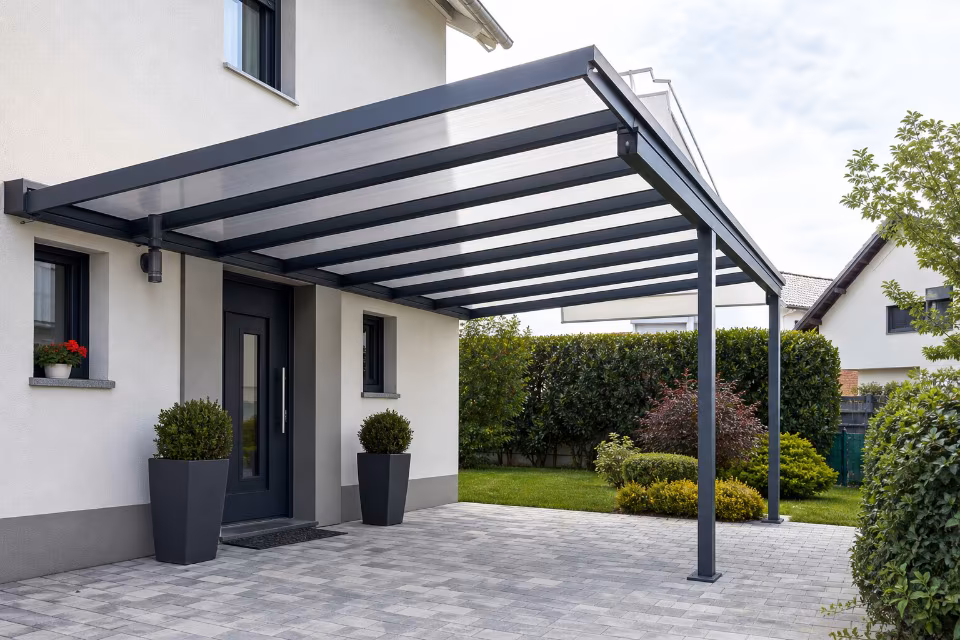Moderna nadstrešnica od aluminija i stakla štiti ulazna vrata od kiše i sunca, elegantno uklopljena u fasadu kuće.