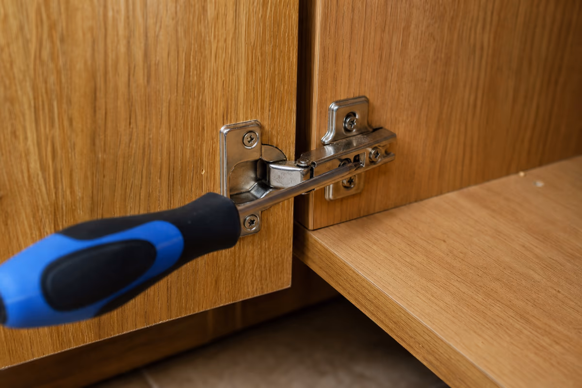 Šrafciger podešava šarku na drvenom ormariću, ilustrirajući preciznost ključnu za montažu i demontažu namještaja pri selidbi