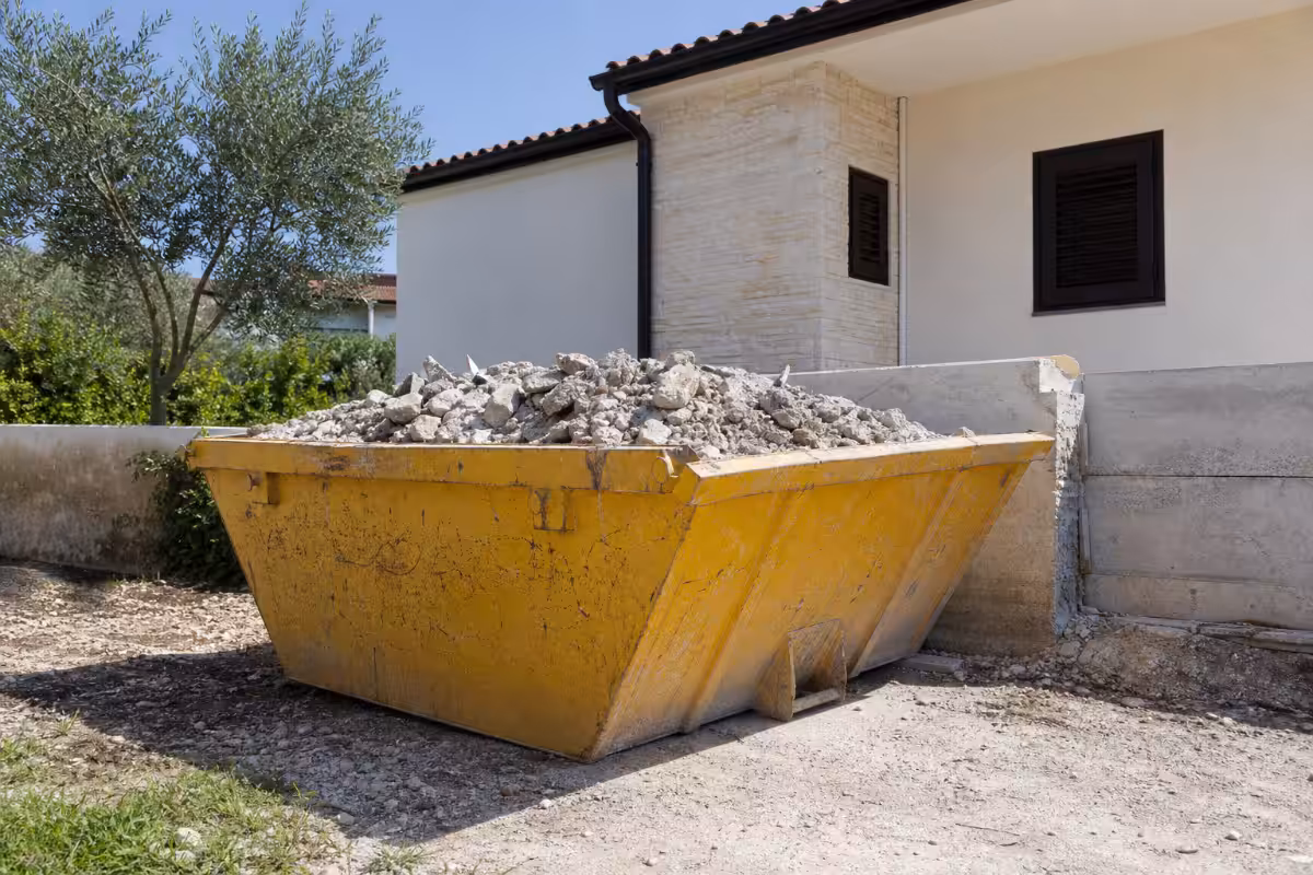 Žuti kontejner za građevinski otpad pun kamenja ispred kuće, ilustracija cene najma
